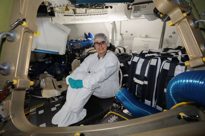 Melanie sitting inside the Starliner crew module. Sbe is wearing protective gear and smiling to camera. 